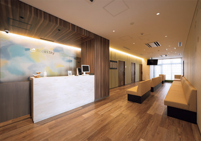 ロビンの空クリニック_1階小児科受付・待合スペースは、木彫仕上げの内装と間接照明で落ち着いた雰囲気を演出